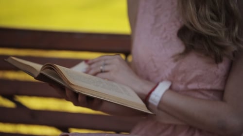 Young Woman Sitting On The Bench In a Park And Reading a Book. Beautiful European Girl Studying