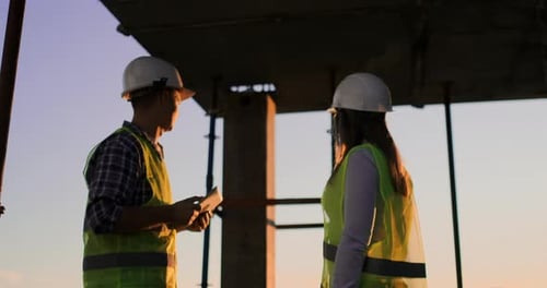 Homme constructeur avec une tablette et une inspectrice dans des casques blancs se serrent la main au coucher du soleil debout