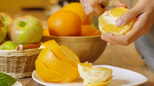 Hands Peeling Orange into Sections at Table