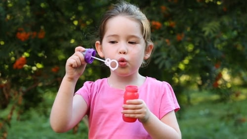 Happy Child Blowing Soap Bubbles In Park