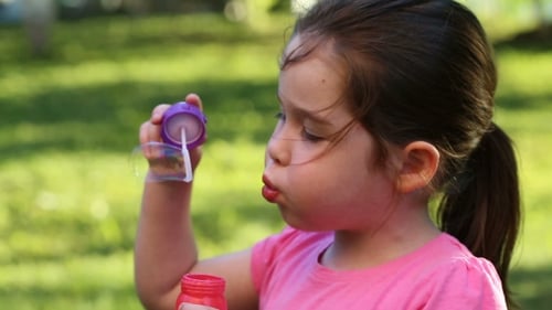 Happy Child Blowing Soap Bubbles In Park