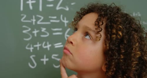 Close-up of thoughtful mixed-race schoolgirl with hand on chin standing in classroom at school 4k