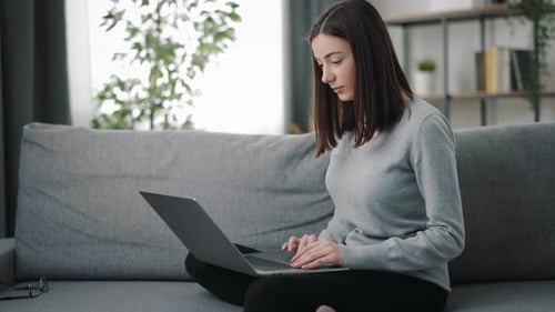 Woman Uses Laptop Computer Sitting on Couch at Home