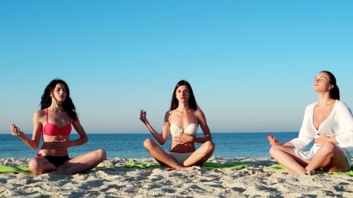 Women Meditating on Beach in Bright Sunlight