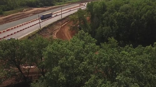 Drohne fliegt von Bäumen und zeigt, wie Kran Rohre für den Straßenbau verlegt