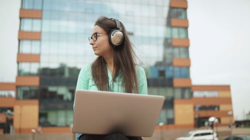 Woman With Laptop and Headphones Outside Office Building
