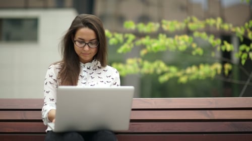 Woman Works on Laptop on Park Bench
