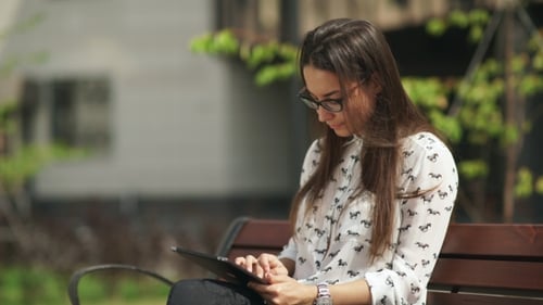 Woman Using Tablet on Bench in Urban Park