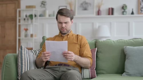 Young Man Reacting to Loss on Documents, Sofa
