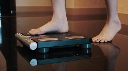 Woman Stand Up On Black Modern Scales In Apartment. Bare Legs. Weighing.