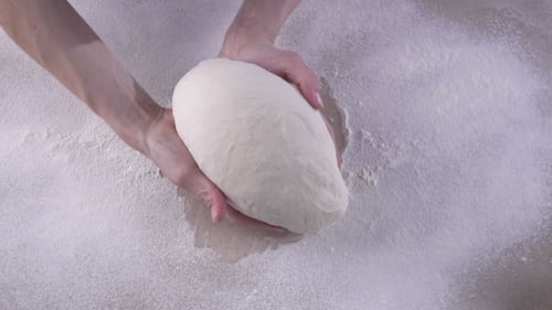 Hands Shaping White Dough on Floured Surface