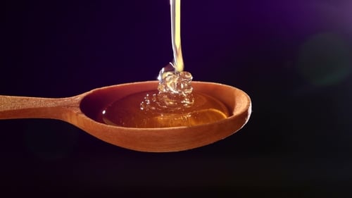 Honey Dripping From a Wooden Honey Dipper On Black, Back Violet Light