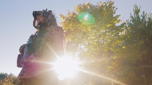 Camouflaged Soldier Stands Outdoors With Rifle in Sunlight