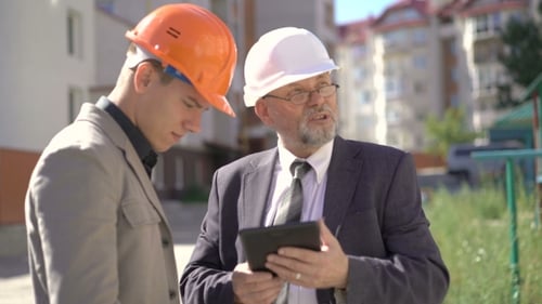 Dos socios comerciales en cascos se reúnen cerca de las construcciones y discutiendo.