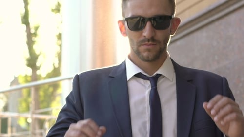 Man Takes Off Sunglasses in City Setting