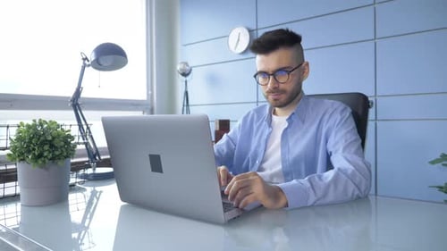 Smiling businessman working on laptop computer at home office. Male professional typing on laptop