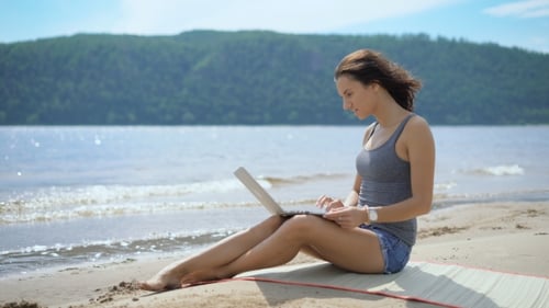 Schöne sexy junge inspirierte Dame sitzt mit Laptop am Strand