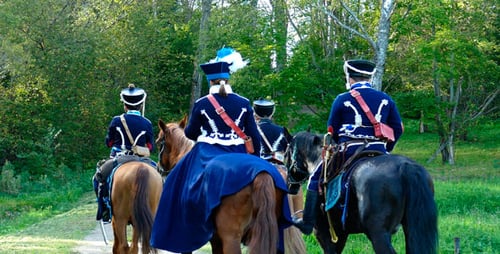 People in Uniforms Ride Horses in the Woods