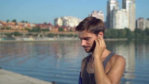 Man Adjusts Headphones Near City Waterfront