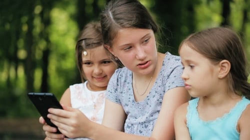 Three Girls Are Fun To Spend Time With a Digital Tablet In a Park.