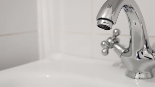 Close Up of Shiny Faucet Running Water in Bathroom