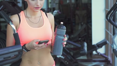 Young Girl Drinking And Using Phone In a Gym