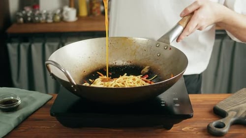 Cook pours sauce into wok with noodles