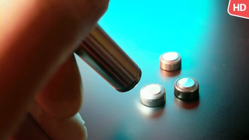 Hand touches button batteries with metallic cylinder