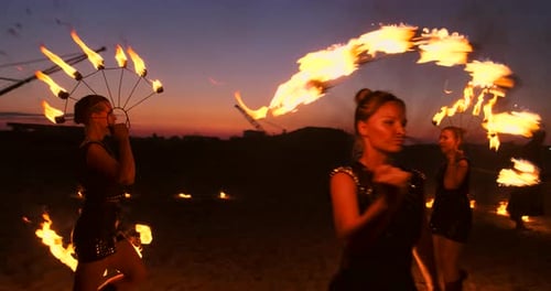 Eine Gruppe von Männern und Frauen Feuershow bei Nacht im Sand vor dem Hintergrund von Feuer und Turm