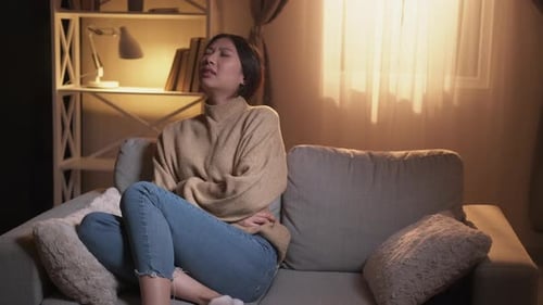 Woman Experiencing Abdominal Pain on Couch at Home