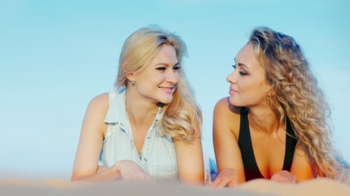 Zwei attraktive sexy Frauen entspannen sich am Strand, liegen im Sand, haben eine gute Zeit