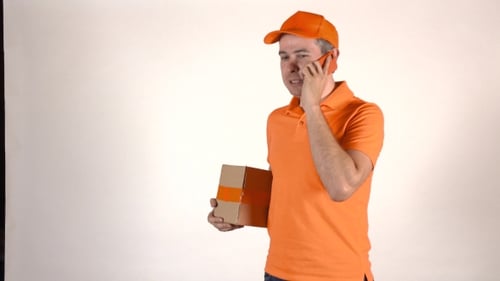 Handsome Courier In Orange Uniform Talking On His Mobile Phone And Delivering a Parcel
