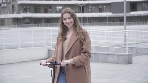 Woman Smiling with Scooter Outdoors in Urban Setting