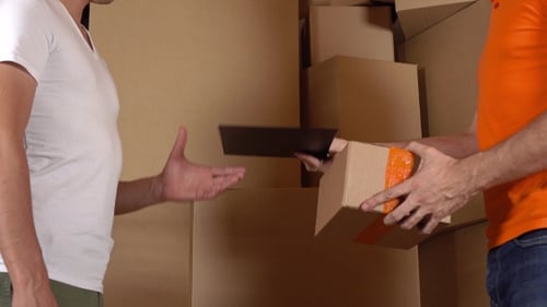Store Assistant In Orange Uniform Giving a Box To a Customer. Cartons Background, Studio Shot