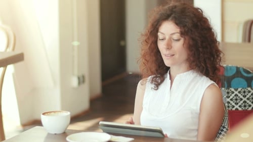 A Woman In a Cafe , Drinking Coffee And Working On The Tablet