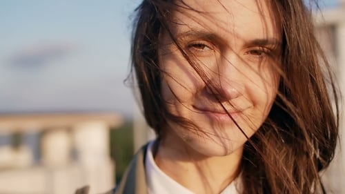 Happy Smiling Woman Standing On The Roof At The Sunset, Looking At Camera Her Long Dark Hair Blowing