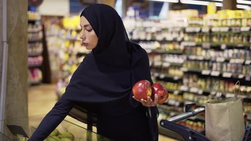 Woman in headscarf shopping for apples in store