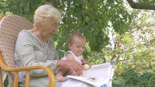 Grandmother Reading Book to Baby Outdoors in Yard