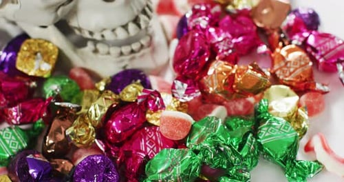 Close up view of human skull and multiple candies fallen against grey background