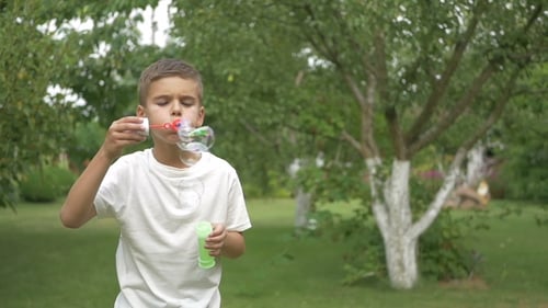 A Cute Boy Blows the Bubbles in the Garden