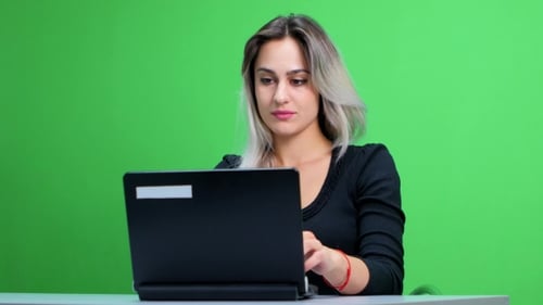 Girl Sitting At The Table And Working At a Laptop. Green Screen Studio