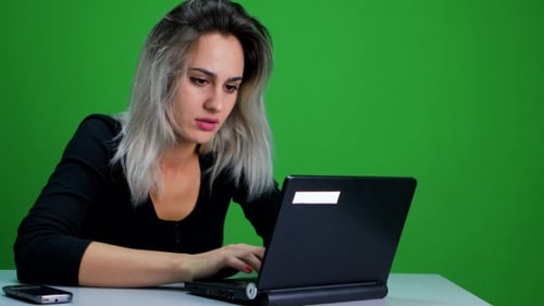 Girl Sitting At The Table And Working At a Laptop. Green Screen Studio
