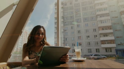 Happy Young Woman Drinking Coffee / Tea And Using Tablet Computer In a Coffee Shop