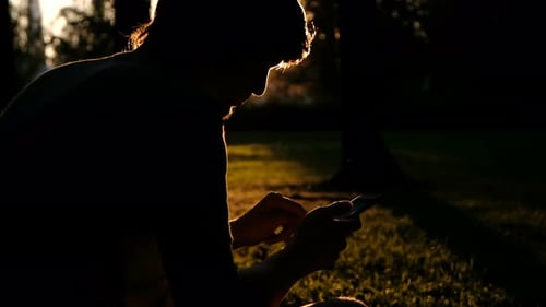 Belle silhouette d'un homme avec un smartphone dans ses mains au coucher du soleil. Relax, Nature Concept