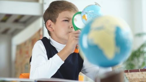 School Boy Examining a Globe With Magnifying Glass