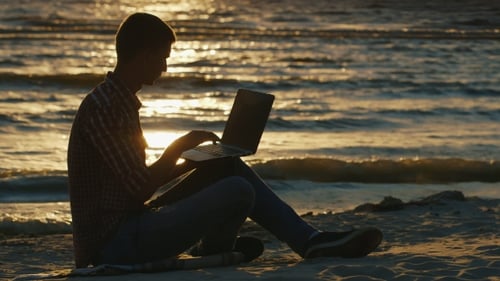 Silhouette Of a Young Man Sitting On The Beach At Sunset