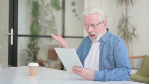 Senior Man Using Tablet Device with Frustration Indoors