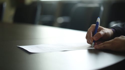 Männliche Unterzeichnung eines Vertrags- oder Abonnementformulars mit einem Stift auf einem rustikalen Holzschreibtisch