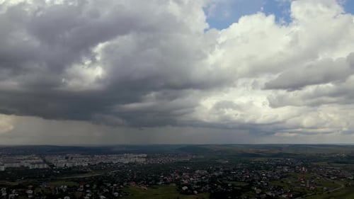 Luftaufnahme aus großer Höhe einer fernen Stadt, die mit geschwollenen Cumuluswolken bedeckt ist, die sich zuvor gebildet haben