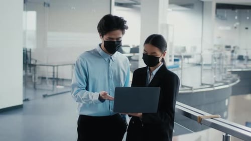 Two Asian Office Workers Using Laptop Talking Wearing Masks Indoor